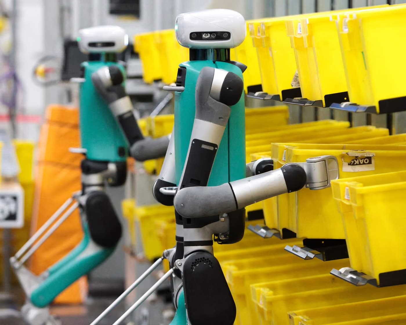 Humanoid robots warehouse floor moving inventory bins between picking zones and storage racks