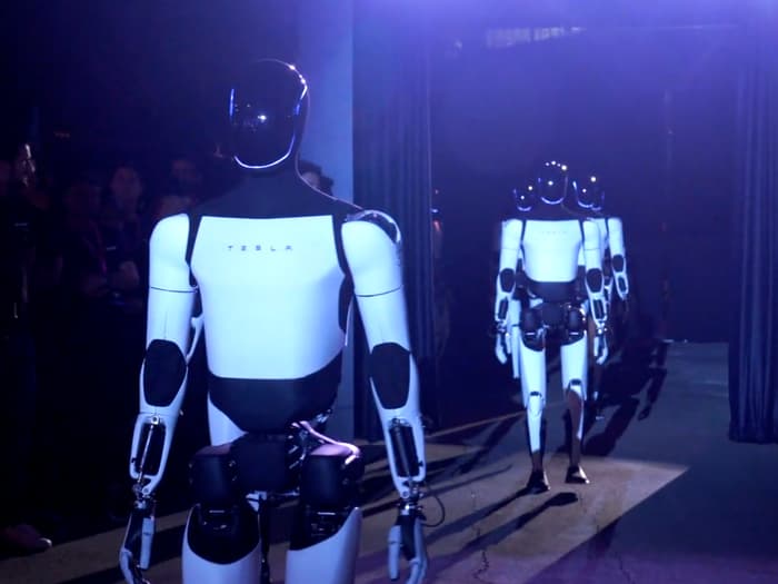 Tesla humanoid robots working on a factory floor beside autonomous vehicles